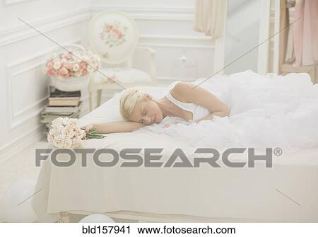 Stock Image - Bride sleeping on bed with bouquet of flowers. Fotosearch