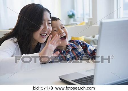 Stock Photo - Brother and sister waving at video chat on computer. Fotosearch