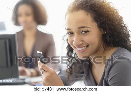 Businesswoman smiling with cell phone in office View Large Photo Image Stock Image - Businesswoman smiling with cell phone in office. Fotosearch