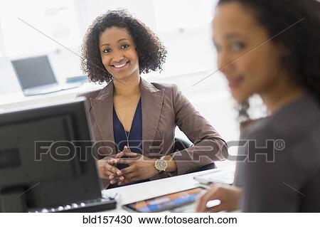 Stock Image - Businesswomen smiling in office meeting. Fotosearch