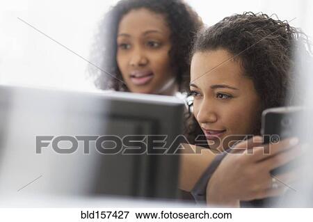 Stock Photo - Businesswomen working with cell phone and computer. Fotosearch
