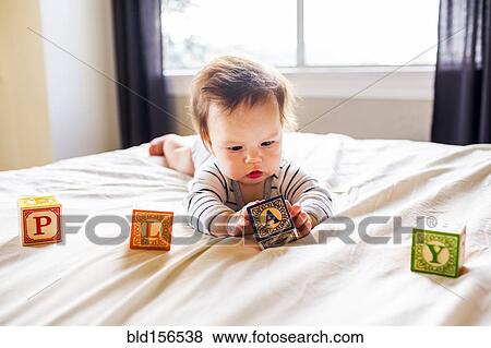 Stock Photo - Caucasian baby girl playing with blocks on bed. Fotosearch