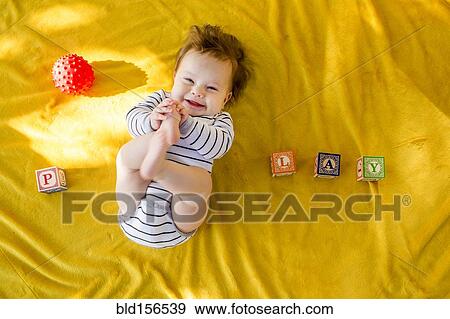 Stock Photo - Caucasian baby girl playing with blocks on bed. Fotosearch