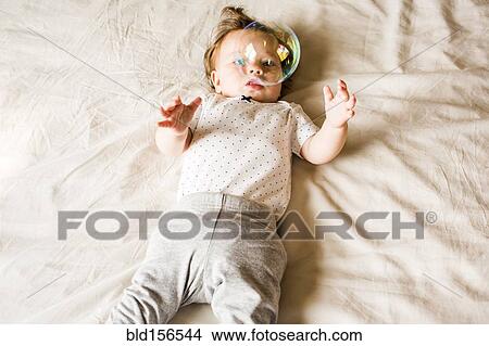 Picture - Caucasian baby girl playing with bubble on bed. Fotosearch