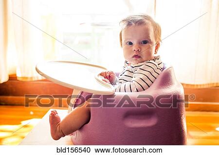 Stock Image - Caucasian baby girl sitting in high chair. Fotosearch
