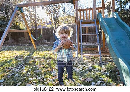 Stock Image - Caucasian boy holding basketball in backyard. Fotosearch
