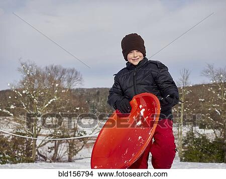 Picture - Caucasian boy holding sled on snowy hill. Fotosearch