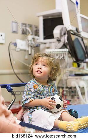 Picture - Caucasian boy sitting on hospital bed with soccer ball. Fotosearch