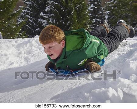 Stock Image - Caucasian boy sledding on snowy hill. Fotosearch
