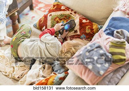 Stock Image - Caucasian boy using cell phone on sofa. Fotosearch