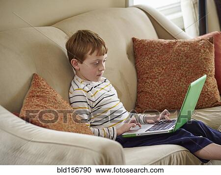 Stock Image - Caucasian boy using laptop on sofa. Fotosearch