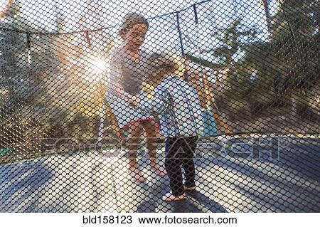 Stock Image - Caucasian brother and sister jumping on trampoline. Fotosearch
