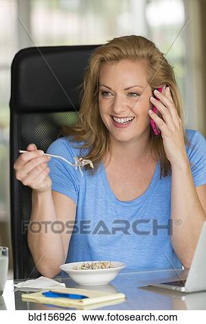 Stock Photograph - Caucasian businesswoman talking on cell phone at breakfast. Fotosearch