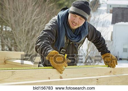 Stock Image - Caucasian carpenter measuring wood planks in winter. Fotosearch
