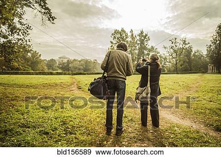 Stock Photo - Caucasian couple standing on trail in park with camera. Fotosearch