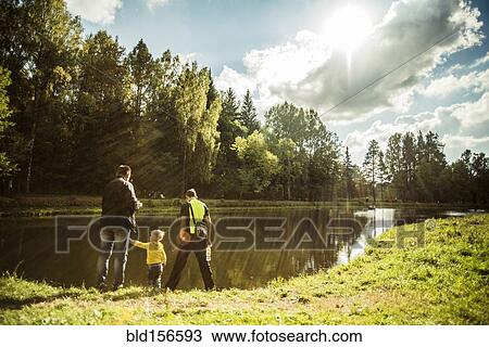 Stock Image - Caucasian father and sons playing near park pond. Fotosearch