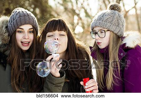 Picture - Caucasian girls blowing bubbles outdoors in winter. Fotosearch