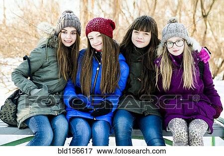 Stock Photo - Caucasian girls smiling on bench in winter. Fotosearch