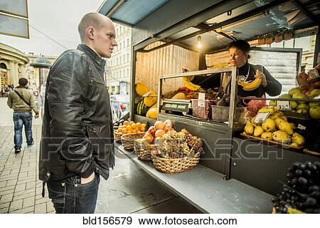 Stock Photo - Caucasian man buying produce at fruit kiosk. Fotosearch