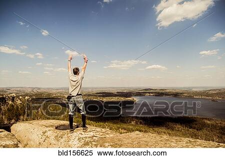 Stock Photography - Caucasian man cheering on remote hilltop. Fotosearch
