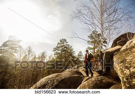 Stock Image - Caucasian man hiking on rock formations in remote forest. Fotosearch