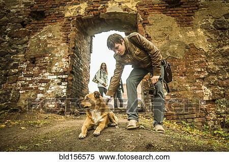 Stock Photography - Caucasian man petting dog near ruins. Fotosearch