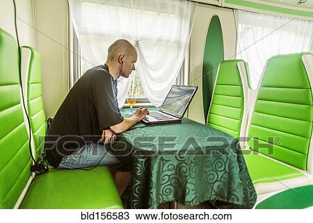 Stock Image - Caucasian man using laptop in green booth on train. Fotosearch
