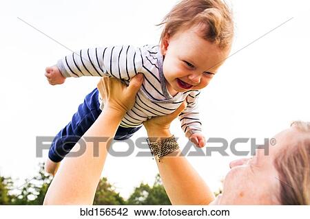 Stock Image - Caucasian mother playing with baby girl outdoors. Fotosearch