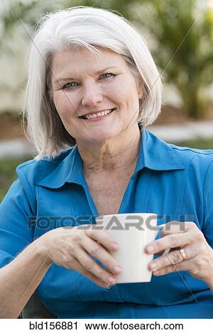 Stock Image - Caucasian older woman drinking coffee outdoors. Fotosearch
