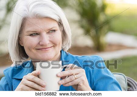 Stock Image - Caucasian older woman drinking coffee outdoors. Fotosearch