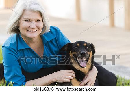 Stock Photograph - Caucasian older woman playing with dog on lawn. Fotosearch