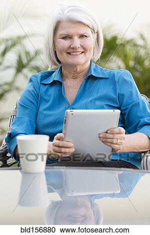 Stock Image - Caucasian older woman using digital tablet in backyard. Fotosearch