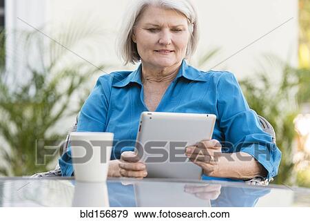 Stock Photo - Caucasian older woman using digital tablet in backyard. Fotosearch
