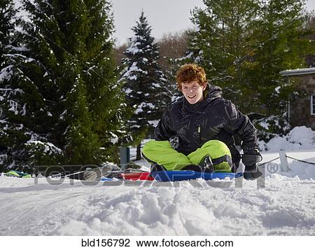 Stock Image - Caucasian teenage boy sledding on snowy hill. Fotosearch