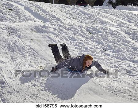 Stock Photography - Caucasian teenage girl sledding on snowy hill. Fotosearch