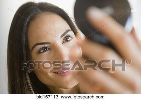 Stock Image - Caucasian woman admiring herself in compact mirror. Fotosearch