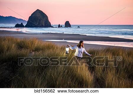 Stock Image - Caucasian woman carrying lantern on Cannon Beach, Oregon, United States. Fotosearch