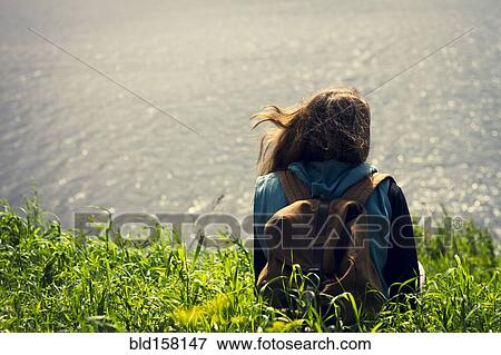 Stock Photo - Caucasian woman laying in grass near lake. Fotosearch