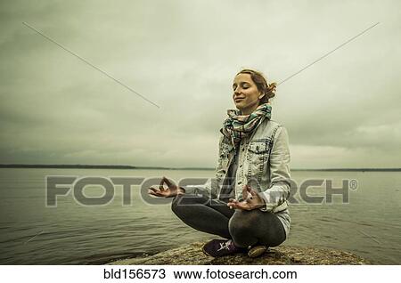 Stock Image - Caucasian woman meditating near ocean. Fotosearch