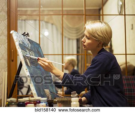 Stock Image - Caucasian woman painting on canvas near mirror. Fotosearch