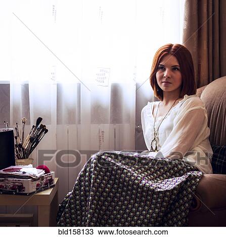 Stock Image - Caucasian woman sitting in armchair near window. Fotosearch