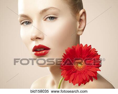 Stock Photography - Caucasian woman with red lipstick holding matching flower. Fotosearch