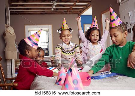 Stock Photograph - Children wearing party hats and celebrating at table. Fotosearch
