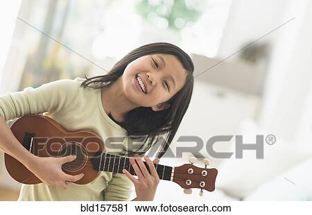 Stock Image - Chinese girl practicing ukulele in bedroom. Fotosearch