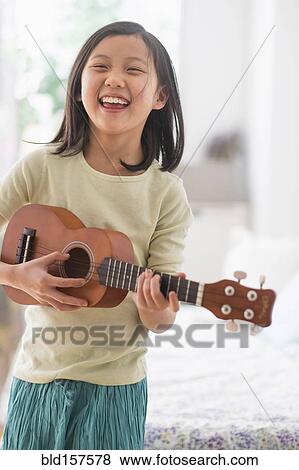 Stock Photo - Chinese girl practicing ukulele in bedroom. Fotosearch