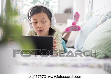 Chinese girl using digital tablet with headphones on bed View Large Photo Image Stock Image - Chinese girl using digital tablet with headphones on bed. Fotosearch
