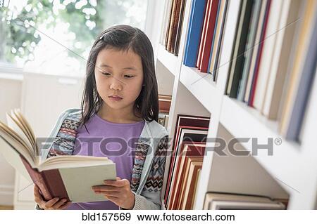 Stock Photo - Chinese student reading book near library bookcase. Fotosearch