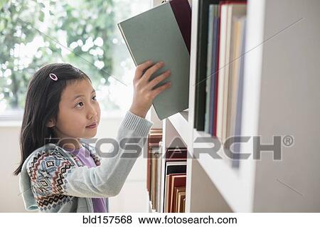 Stock Photo - Chinese student selecting book from library bookcase. Fotosearch