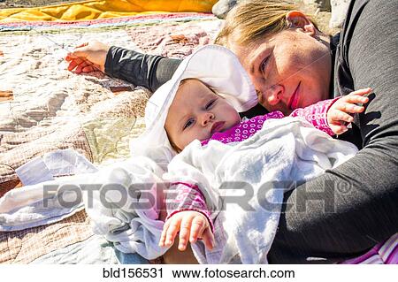 Stock Image - Close up of Caucasian mother and baby girl laying on blanket. Fotosearch