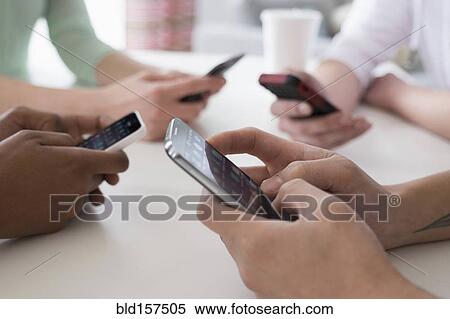 Stock Photography - Close up of friends texting on cell phones at table. Fotosearch